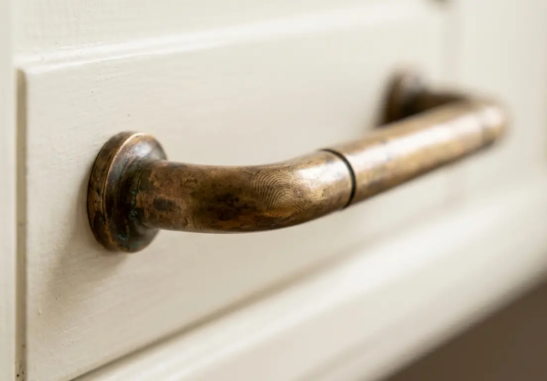 Macro shot of an aged unlacquered brass pull with warm patina on a cream painted cabinet door