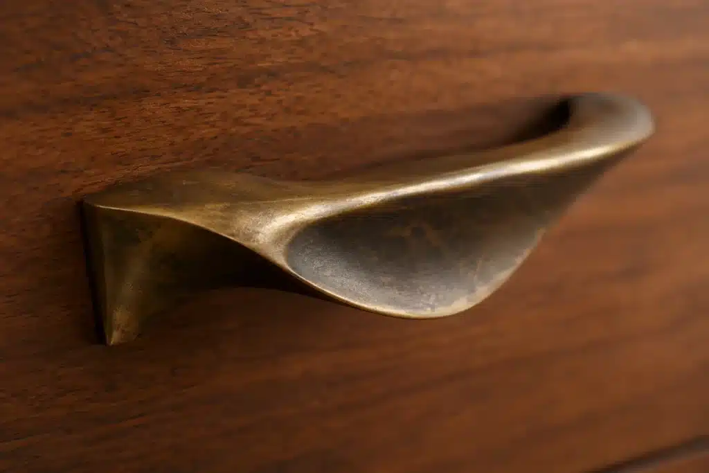 Macro close-up of a vintage mid-century modern brass drawer pull showing a rich amber-bronze patina on walnut wood