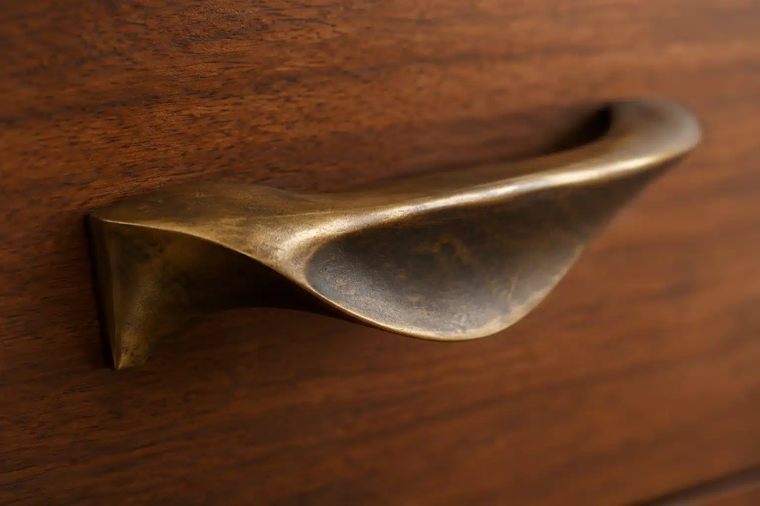 Macro close-up of a vintage mid-century modern brass drawer pull showing a rich amber-bronze patina on walnut wood